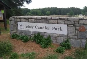 Stone entrance sign for Murphey Candler Park in DeKalb County with a lake behind.