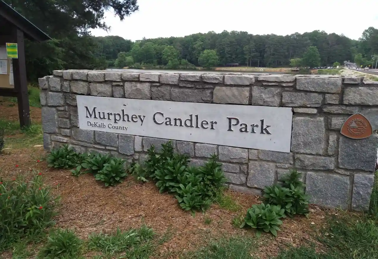 Stone entrance sign for Murphey Candler Park in DeKalb County with a lake behind.