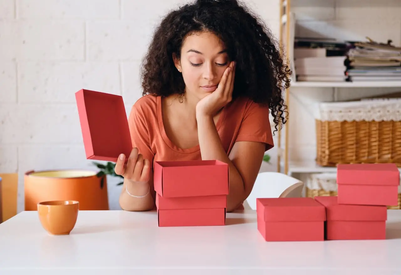 Thoughtful young woman opening small red boxes on a white table.
